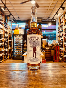 Redwood Empire Bourbon Whiskey 750mL a large long necked clear glass bottle with a large white label and the image of a man with leaves as his head and a wooden top 