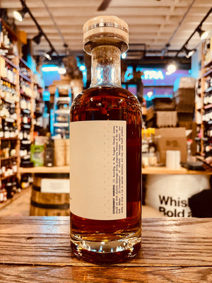 Wolves Rye Project #1 750mL side of a short clear round shouldered clear glass bottle with a white label and a wooden top