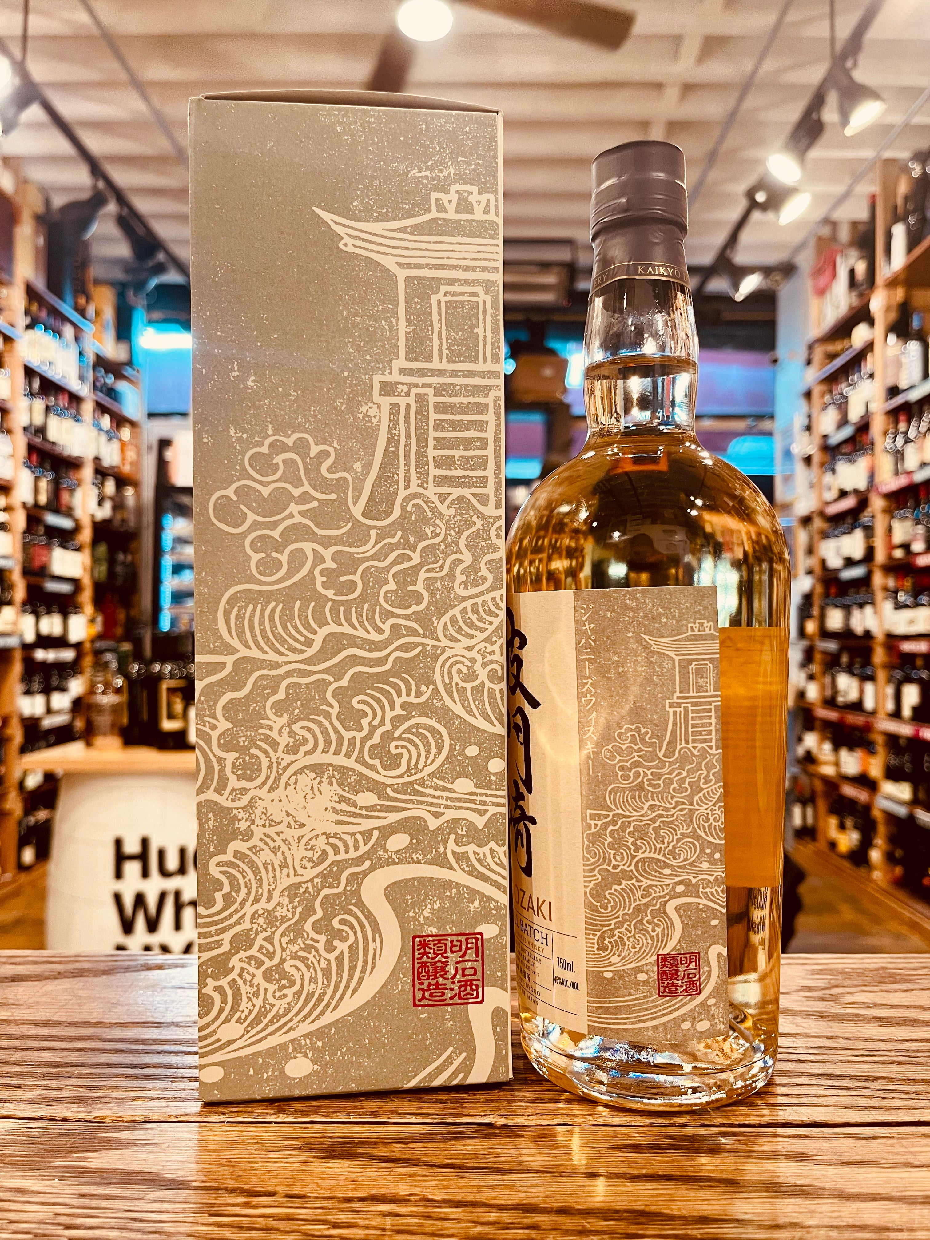 Hatozaki Small Batch Japanese Whisky 750mL the backside of a tall box gray with an image of a Japanese tower on it, next to a clear rounded shouldered bottle with the same image