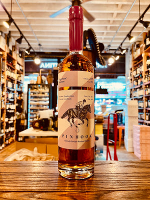 Pinhook 2023 High Proof Bourbon 750mL a tall clear glass bottle with a slender long neck with a pink and white label an image of a jockey riding a horse with a waxed purple top
