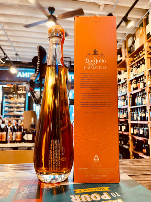 Don Julio Reposado Primavera 750mL the back side of a tall thin clear bottle with a wooden top next to a tall thing orange bottle