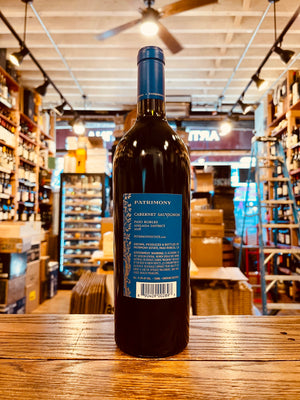 Patrimony Cabernet Sauvignon 750mL 2018 the backside of a tall dark wine bottle with a blue label and blue top