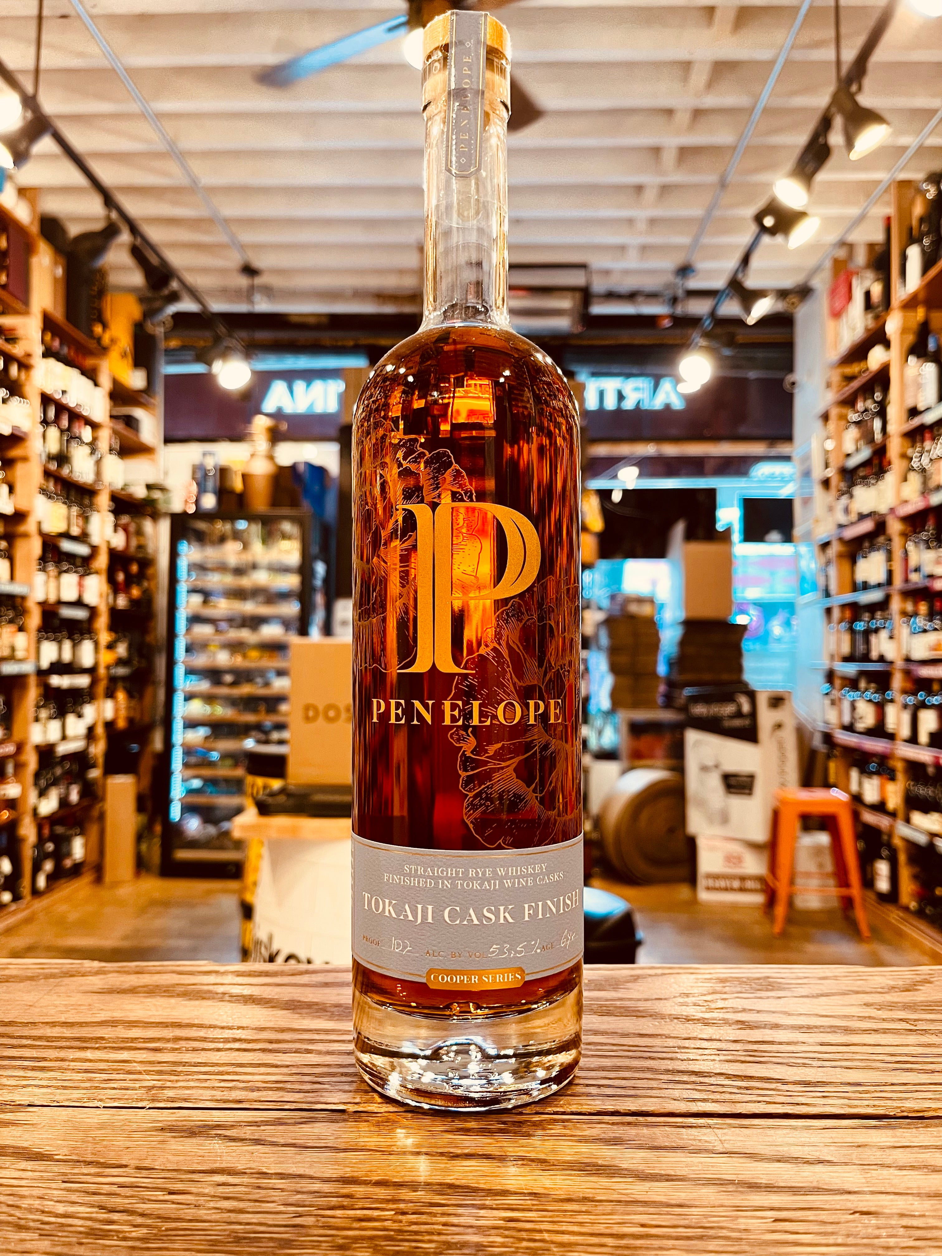 Penelope Rye Tokaji Cask 750mL a tall clear glass bottle with a long neck and a light blue label at the bottom and a big gold P printed on the front 