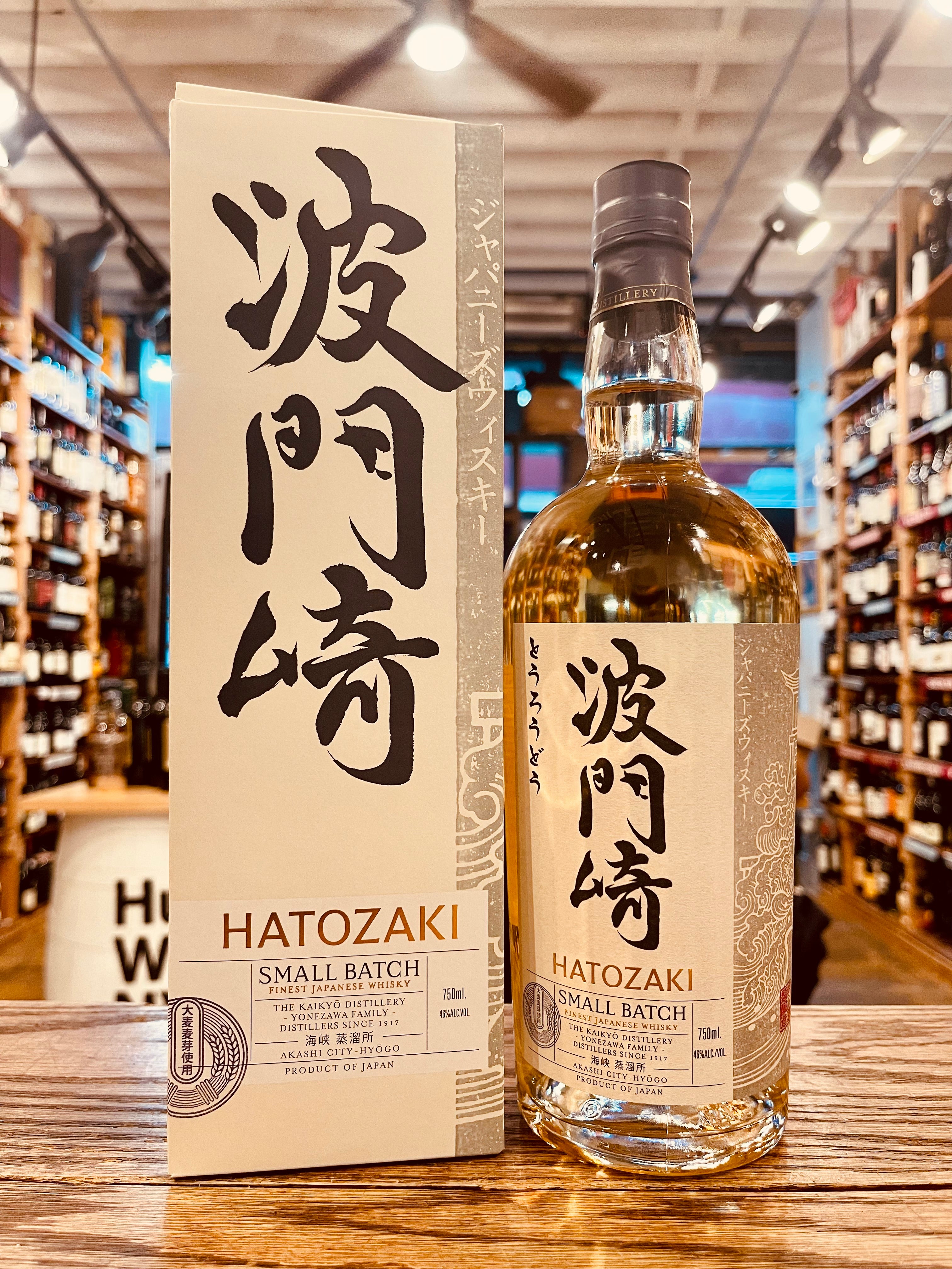 Hatozaki Small Batch Japanese Whisky 750mL a tall squared white box with black Japanese symbols on it next to a tall rounded shouldered clear bottle with a white label and Japanese symbols on it.