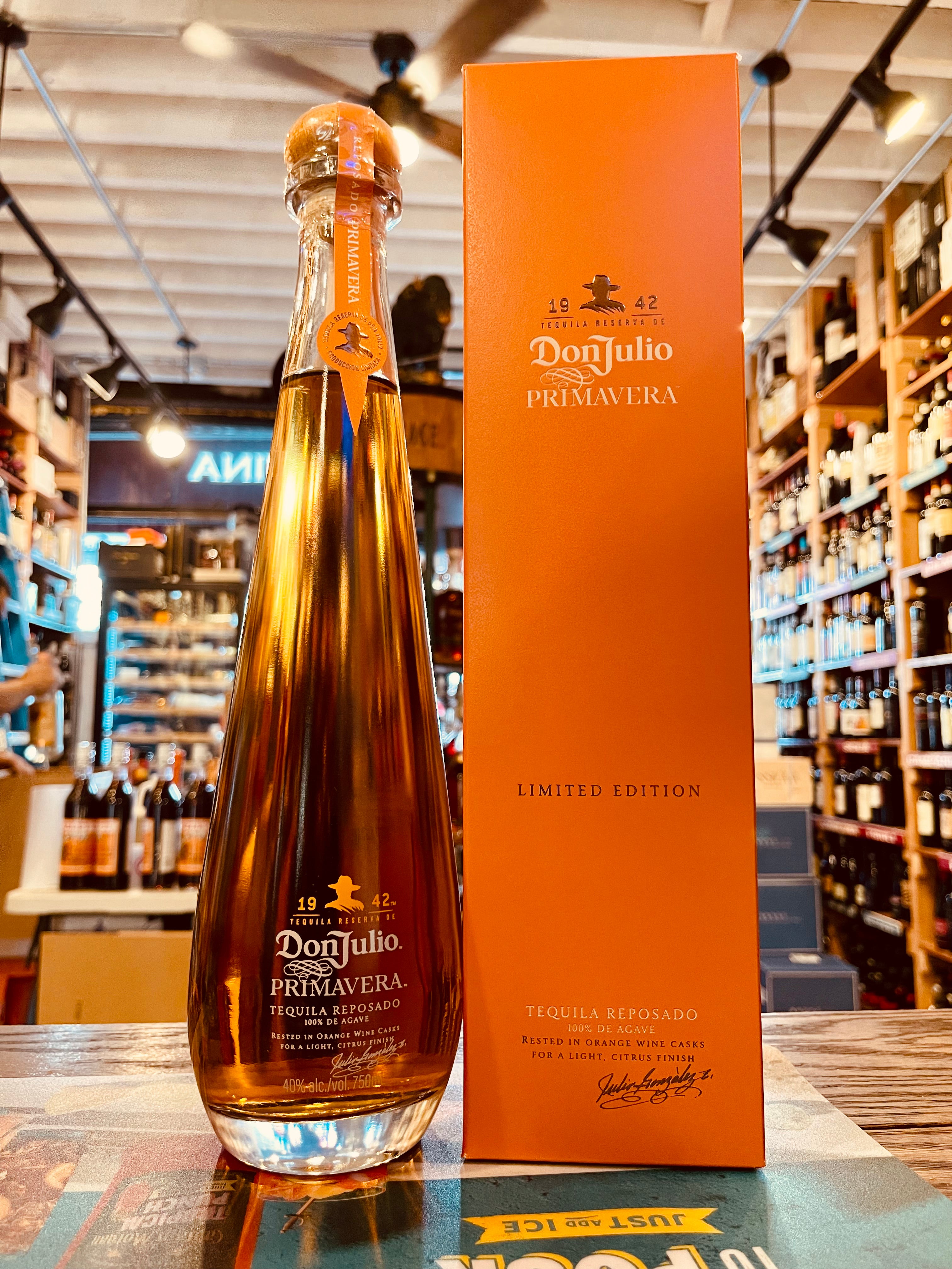 Don Julio Reposado Primavera 750mL a tall clear long bottle with white lettering and a wooden top next to a tall thin orange box