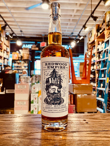 Redwood Empire American Whiskey 750mL a tall long necked clear glass bottle with a large white label with the image of a man's head with trees growing from it and a wooden top