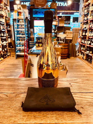 Armand de Brignac Champagne Brut Ace of Spades Gold 750 mL tall golden bottle with a black top next to a black sack