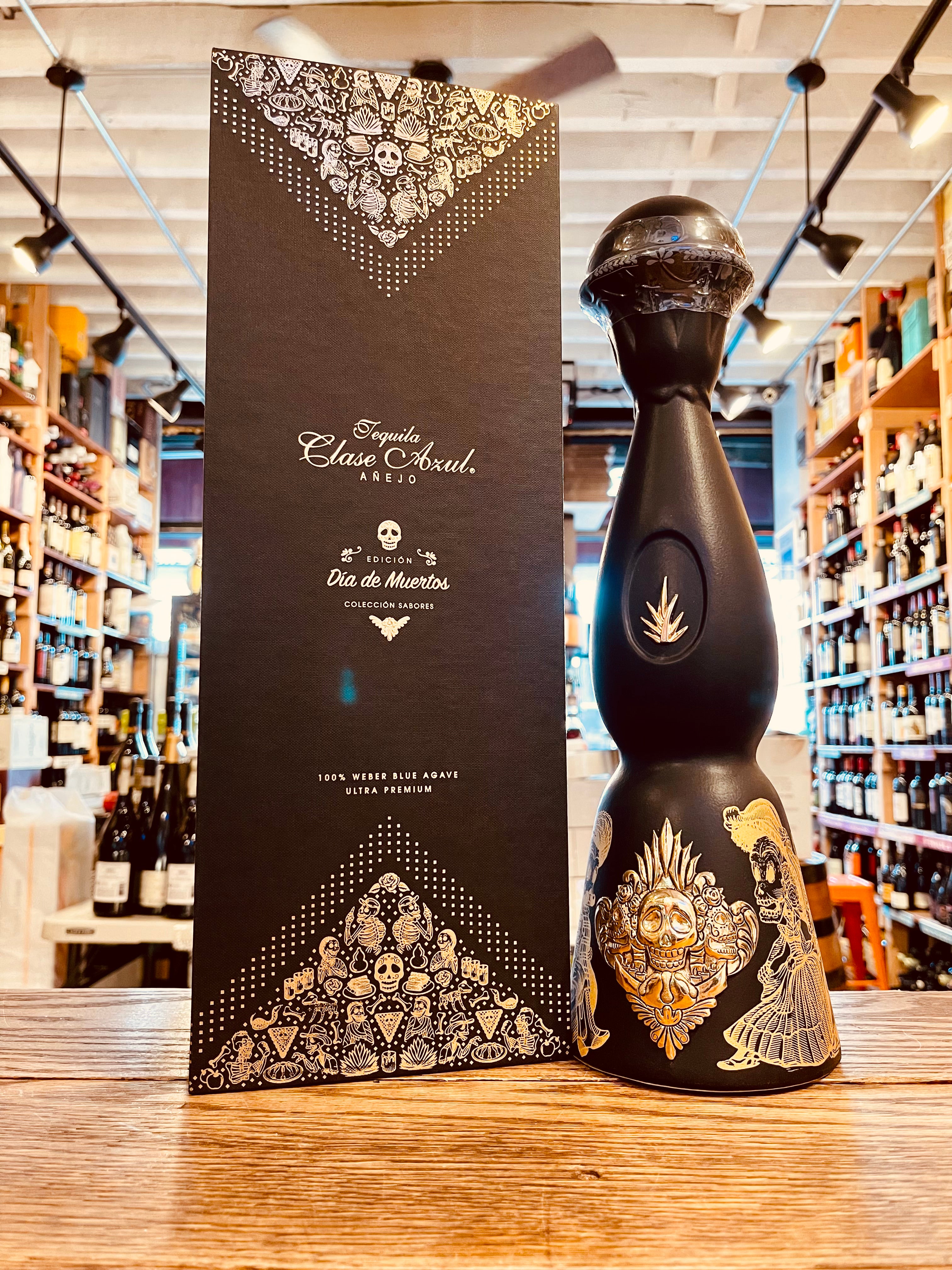 Clase Azul Dia De Los Muertos 1L a tall elegantly designed black bottle with a gold plated design of skeletons besides a tall black box with gold lettering  