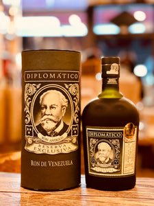 Diplomatico Reserva Exclusiva 750mL a black cylinder with an old man's face on it next to a small squat dark bottle with a short neck and white label, also with the old man's face on it 