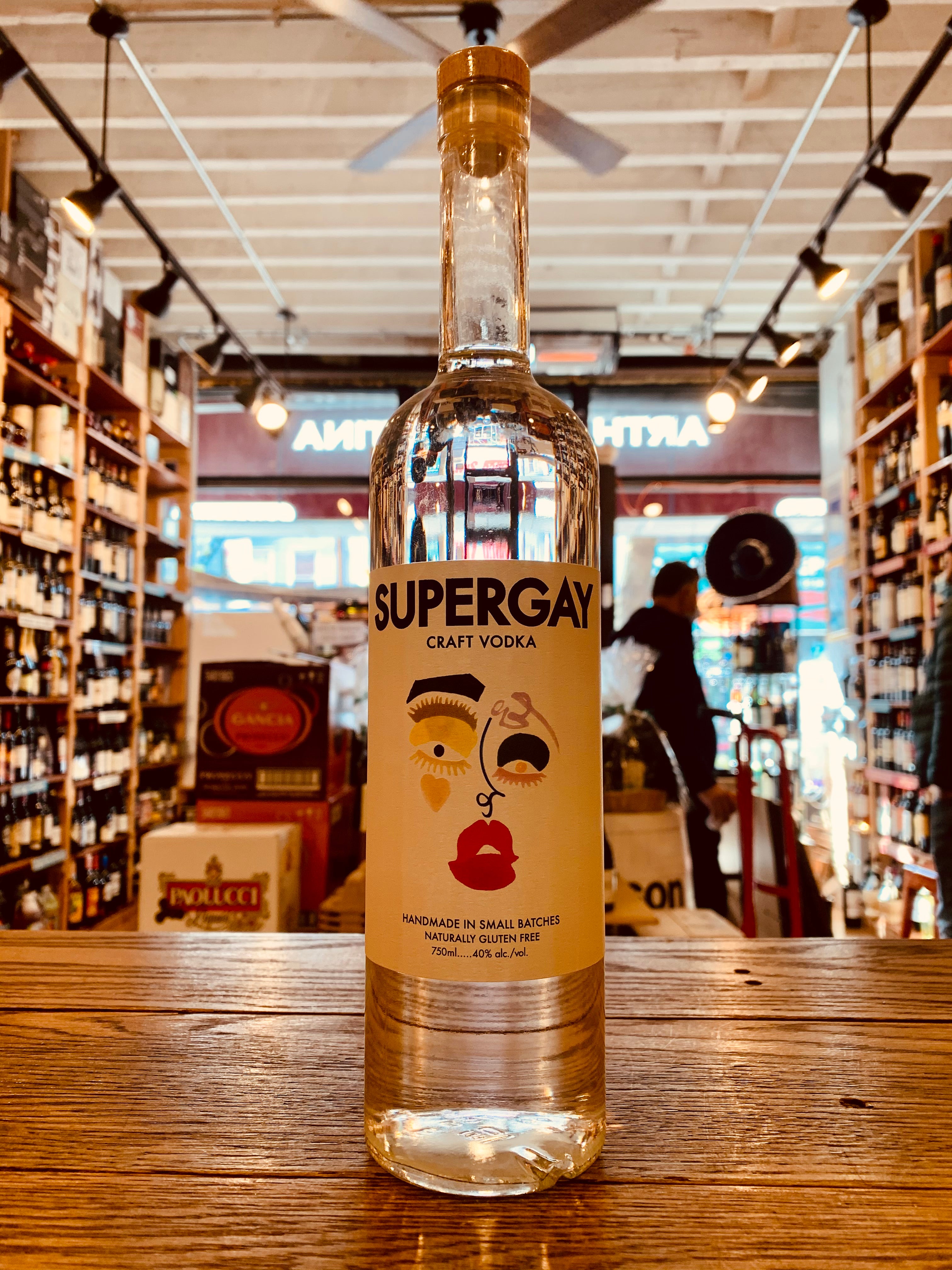 Super Gay Craft Vodka 750mL a tall slender long necked clear glass bottle with a white label with the image of a face on it and a wooden top