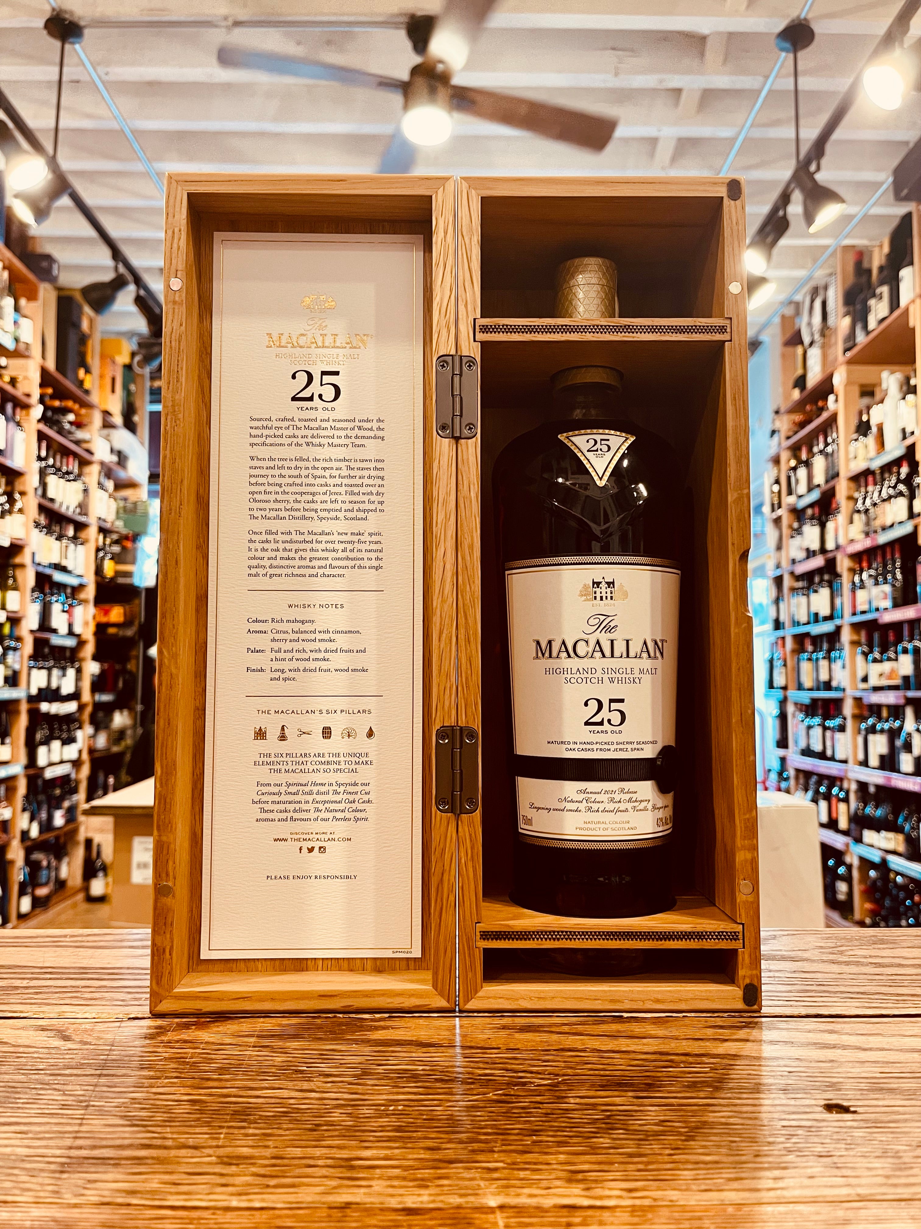 Macallan 25Yr Sherry Oak 750mL an open wooden box with a white leaflet inside it with a tall clear glass bottle with a white label and golden top