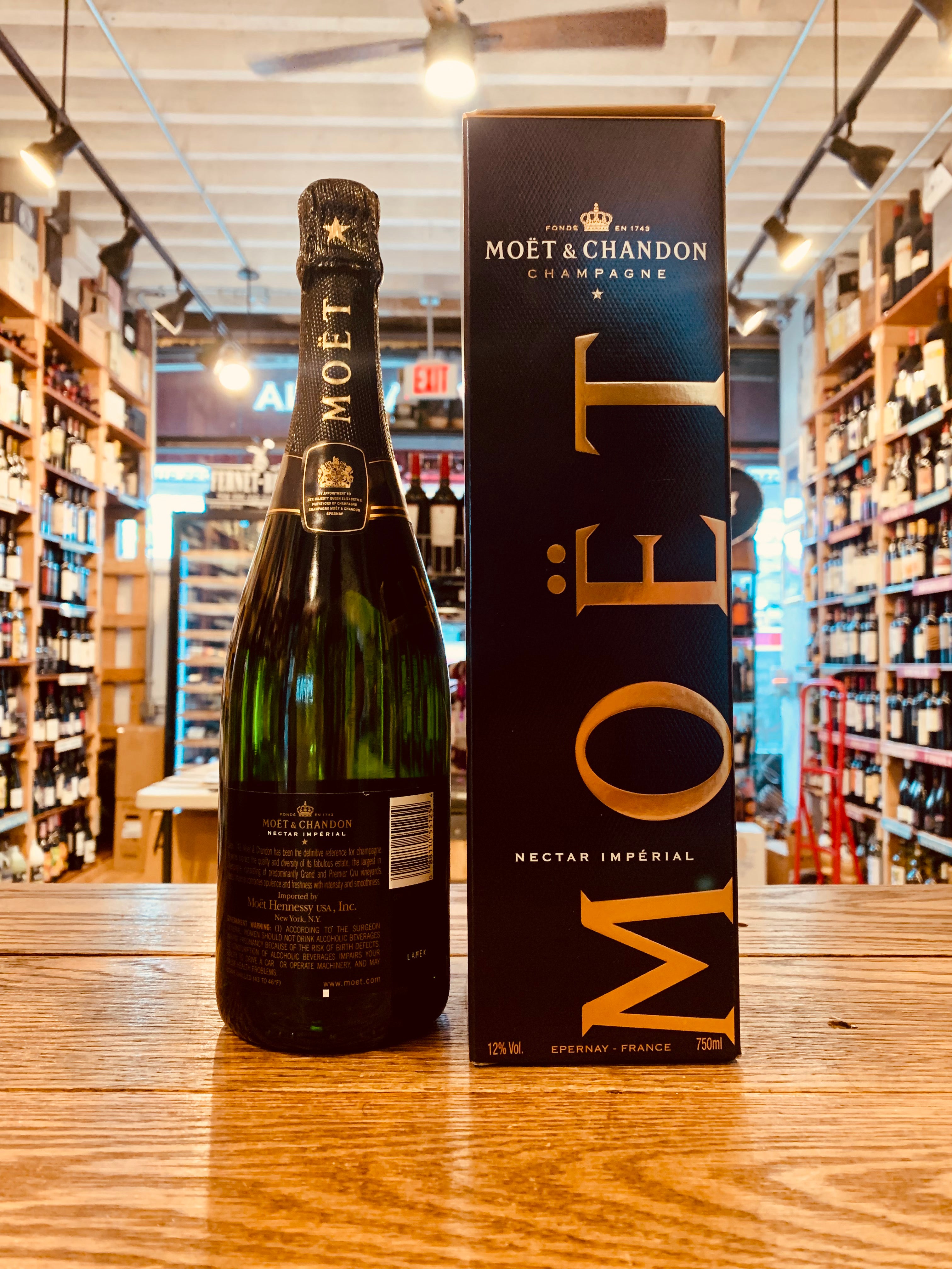 Moet Nectar Imperial 750mL the backside of a dark green clear glass bottle with a black and gold label with a golden top next to a tall black box with golden lettering