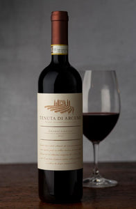 Tenuta di Arceno Chianti Classico 750mL a tall dark glass wine bottle with a beige label and a maroon top next to a glass of red wine