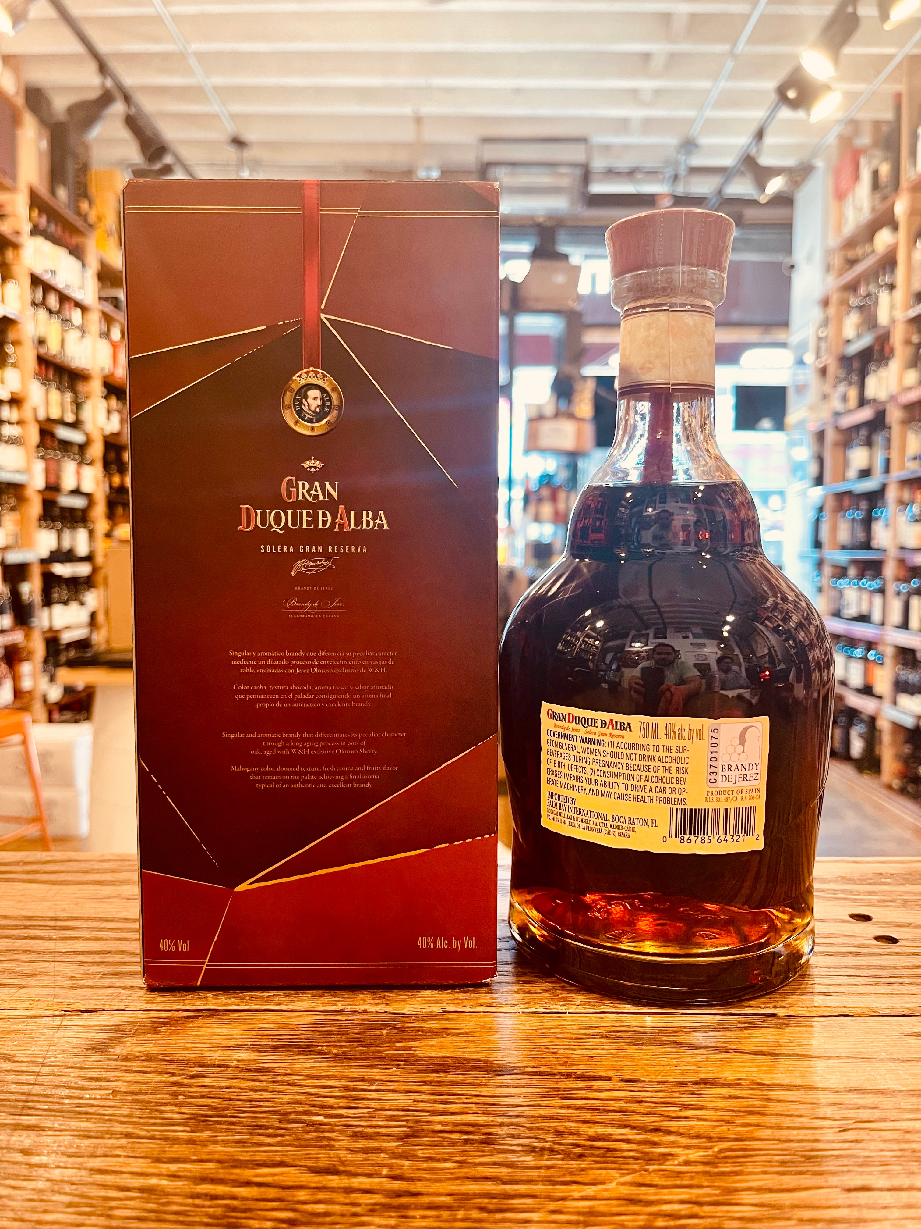 Gran Duque D'Alba Gran Reseva 750mL the backside of a red box with the image of a man's face on it next to a small squat rounded clear bottle with a yellow label and red top